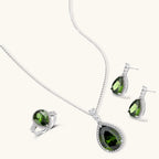 White gold plated jewelry set with green teardrop gemstones and cubic zirconia halos on cream background.