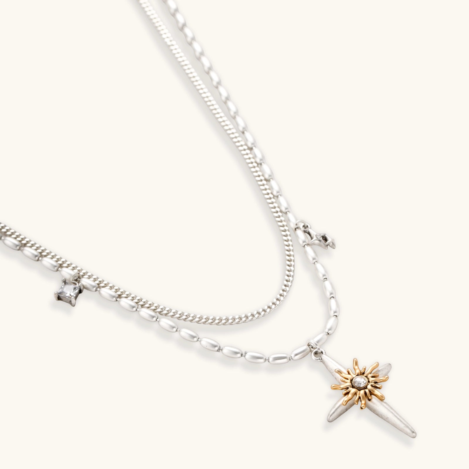 Two-layer silver-toned necklace with star charms and dagger pendant featuring golden sun motif on white background.