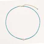 Delicate gold vermeil necklace with teal apatite beads and freshwater pearl on white background.