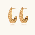 Curved gold hoop earrings with raised granulated texture resembling sea urchin surface on cream background