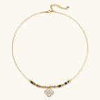 Gold-toned beaded necklace with grey stones and quatrefoil abalone shell pendant on cream background.