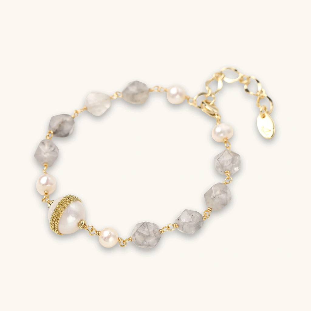 Bracelet with cloudy quartz beads, freshwater pearls, and gold-wrapped baroque pearl centerpiece on white background.