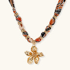 Vibrant patterned fabric necklace with gold-toned flower pendant featuring rhinestone center on white background