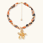 Vibrant patterned fabric necklace with gold-toned flower pendant featuring rhinestone center on white background