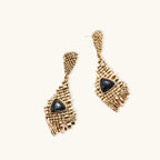 Gold-toned geometric mesh earrings with black triangular resin stones and fringe detail on neutral background