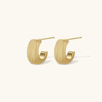 Small gold huggie earrings with matte finish, 14mm diameter, shown against cream background for everyday elegance.