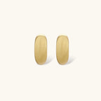 Small gold huggie earrings with matte finish, 14mm diameter, shown against cream background for everyday elegance.