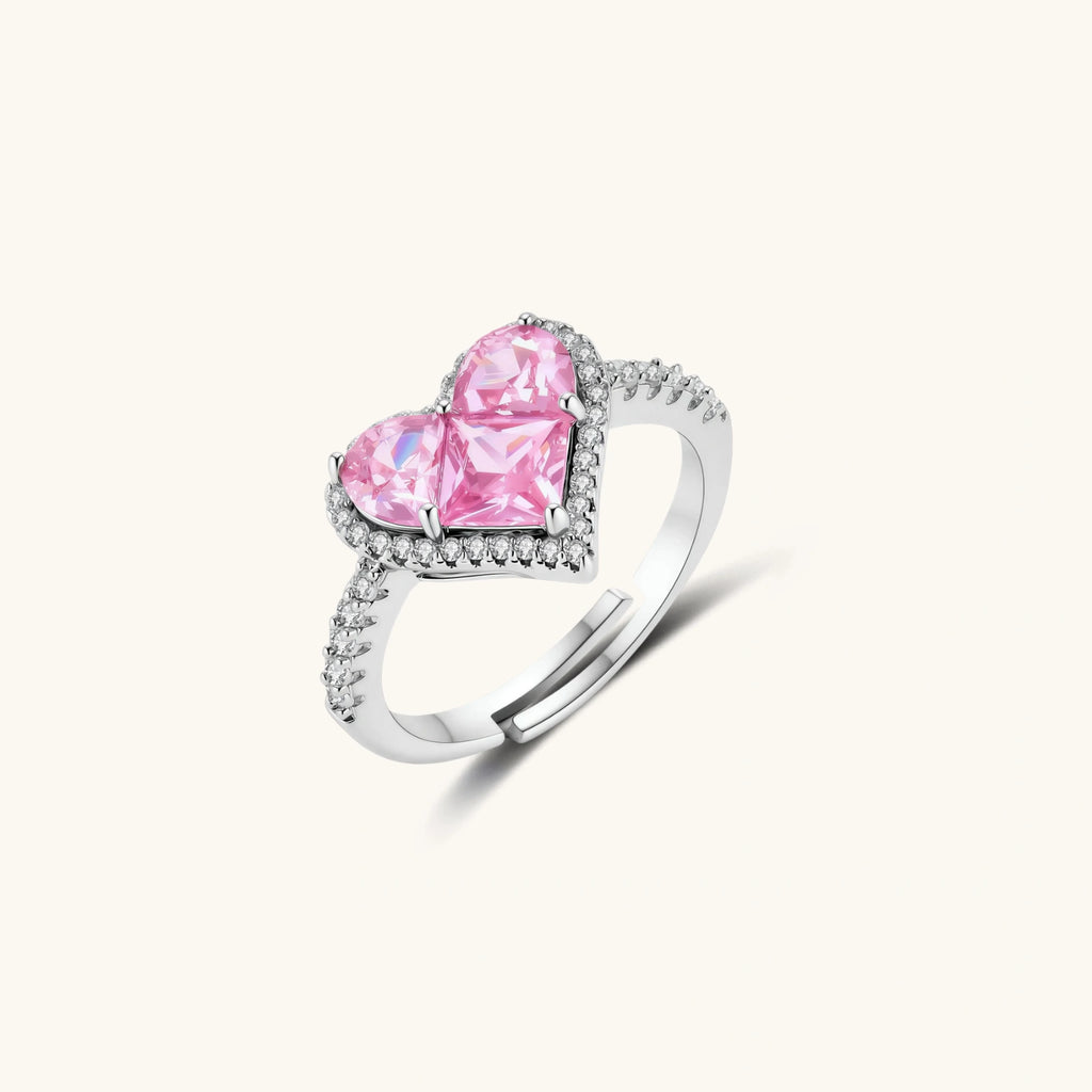 Heart-shaped ring with pink zirconia stones in white gold-plated setting, adjustable band on neutral background.
