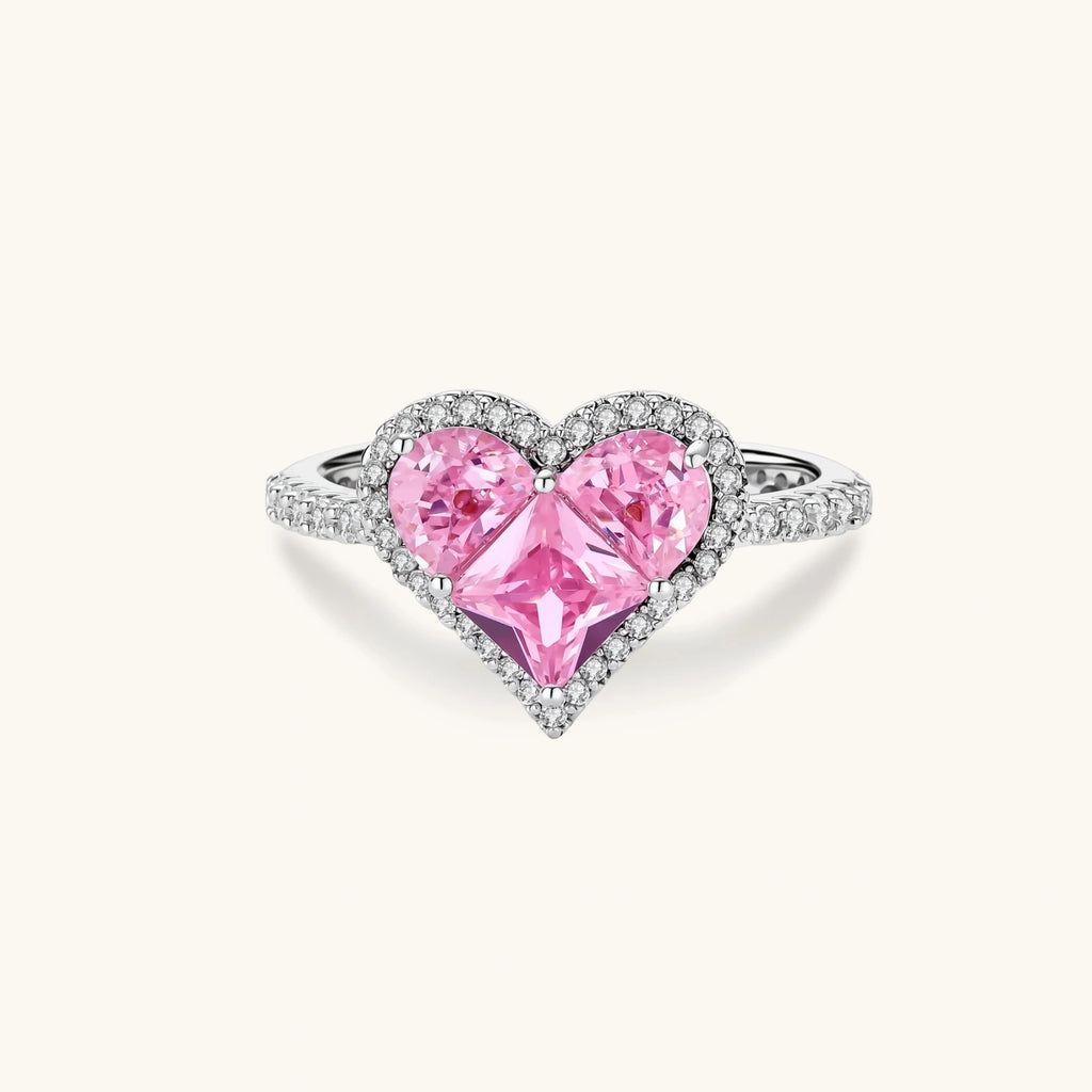Heart-shaped ring with pink zirconia stones in white gold-plated setting, adjustable band on neutral background.