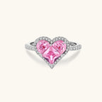 Heart-shaped ring with pink zirconia stones in white gold-plated setting, adjustable band on neutral background.