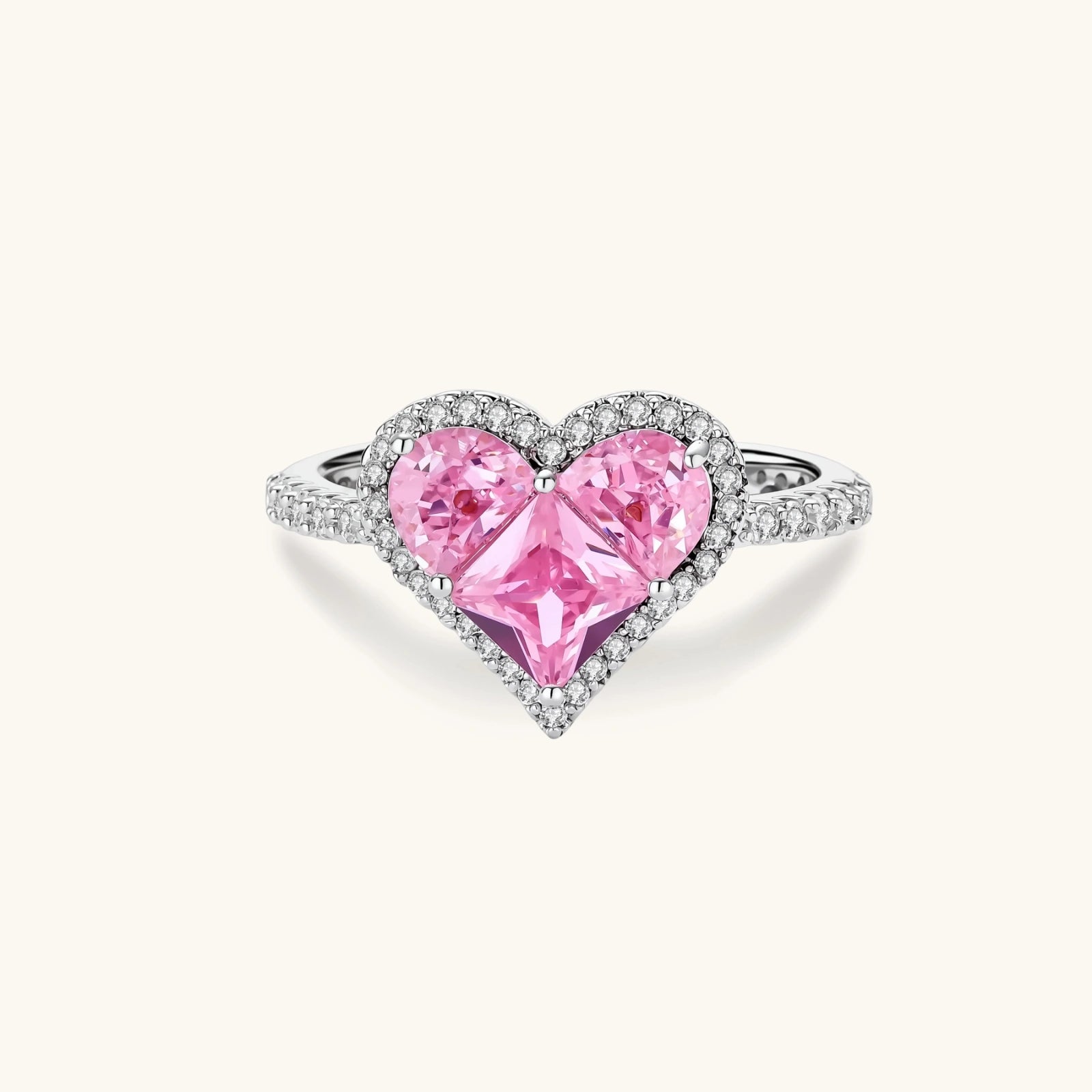 Heart-shaped ring with pink zirconia stones in white gold-plated setting, adjustable band on neutral background.