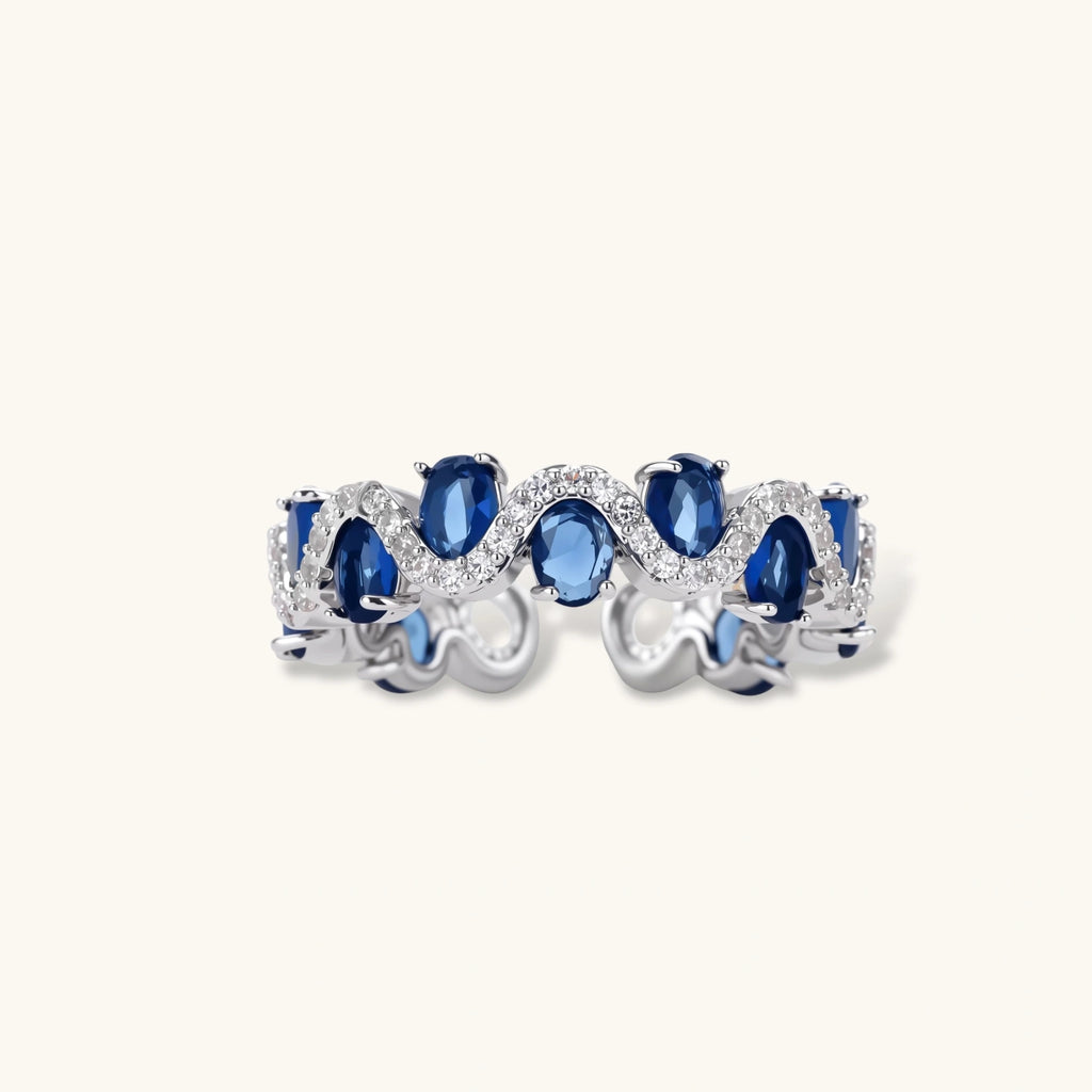 Adjustable ring with blue cubic zirconia stones in flowing wave pattern, copper with platinum plating on white background.
