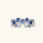 Adjustable ring with blue cubic zirconia stones in flowing wave pattern, copper with platinum plating on white background.