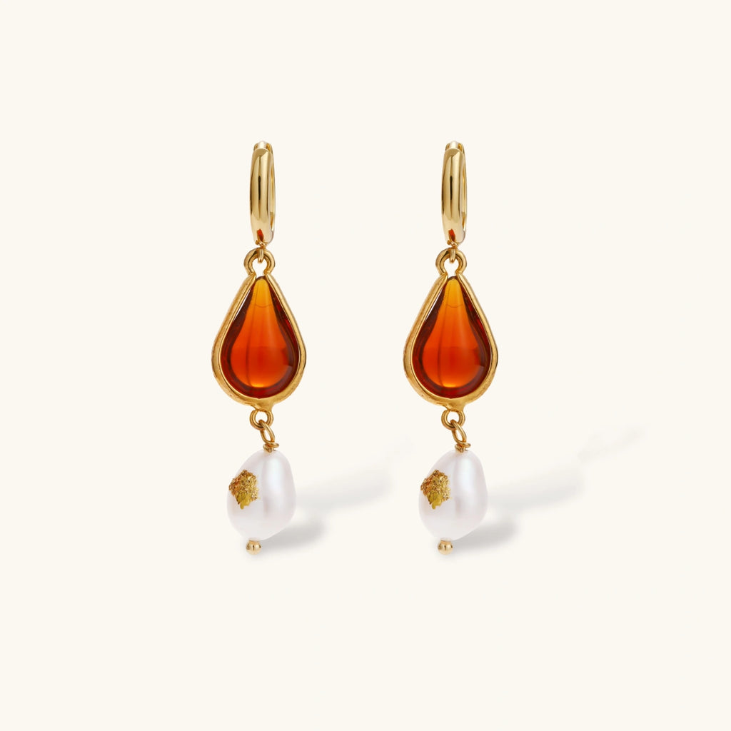 Gold-plated drop earrings featuring amber teardrops and white baroque pearls on light background.
