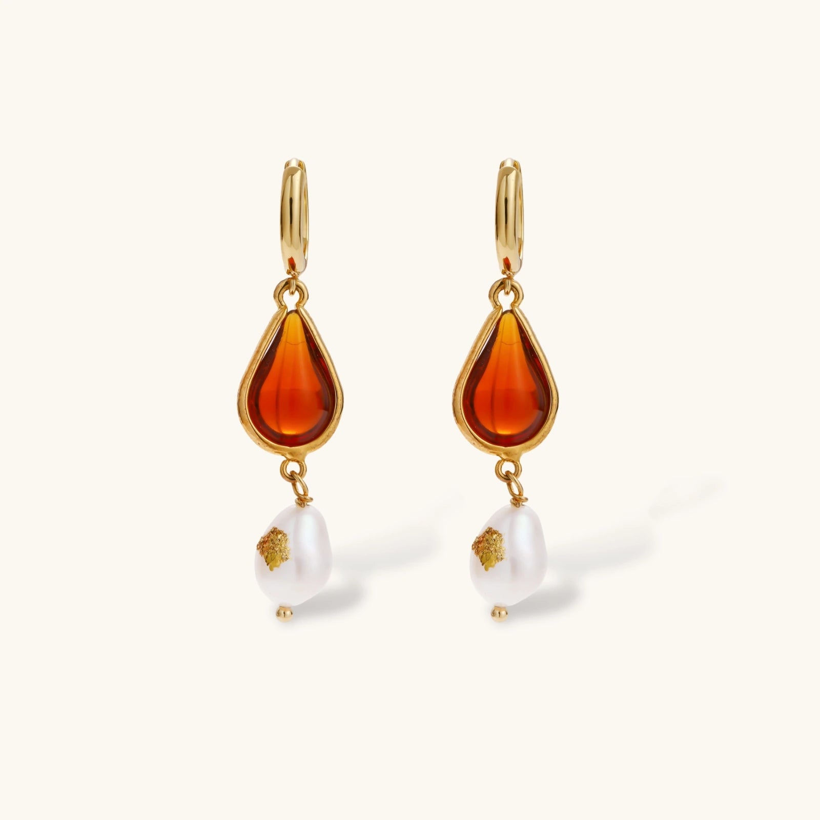 Gold-plated drop earrings featuring amber teardrops and white baroque pearls on light background.