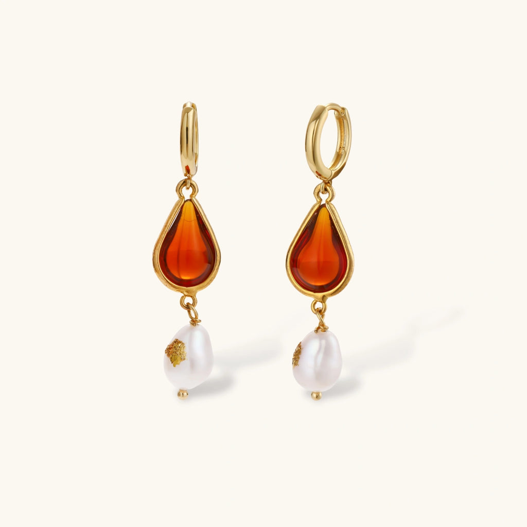 Gold-plated drop earrings featuring amber teardrops and white baroque pearls on light background.