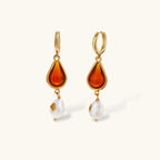 Gold-plated drop earrings featuring amber teardrops and white baroque pearls on light background.