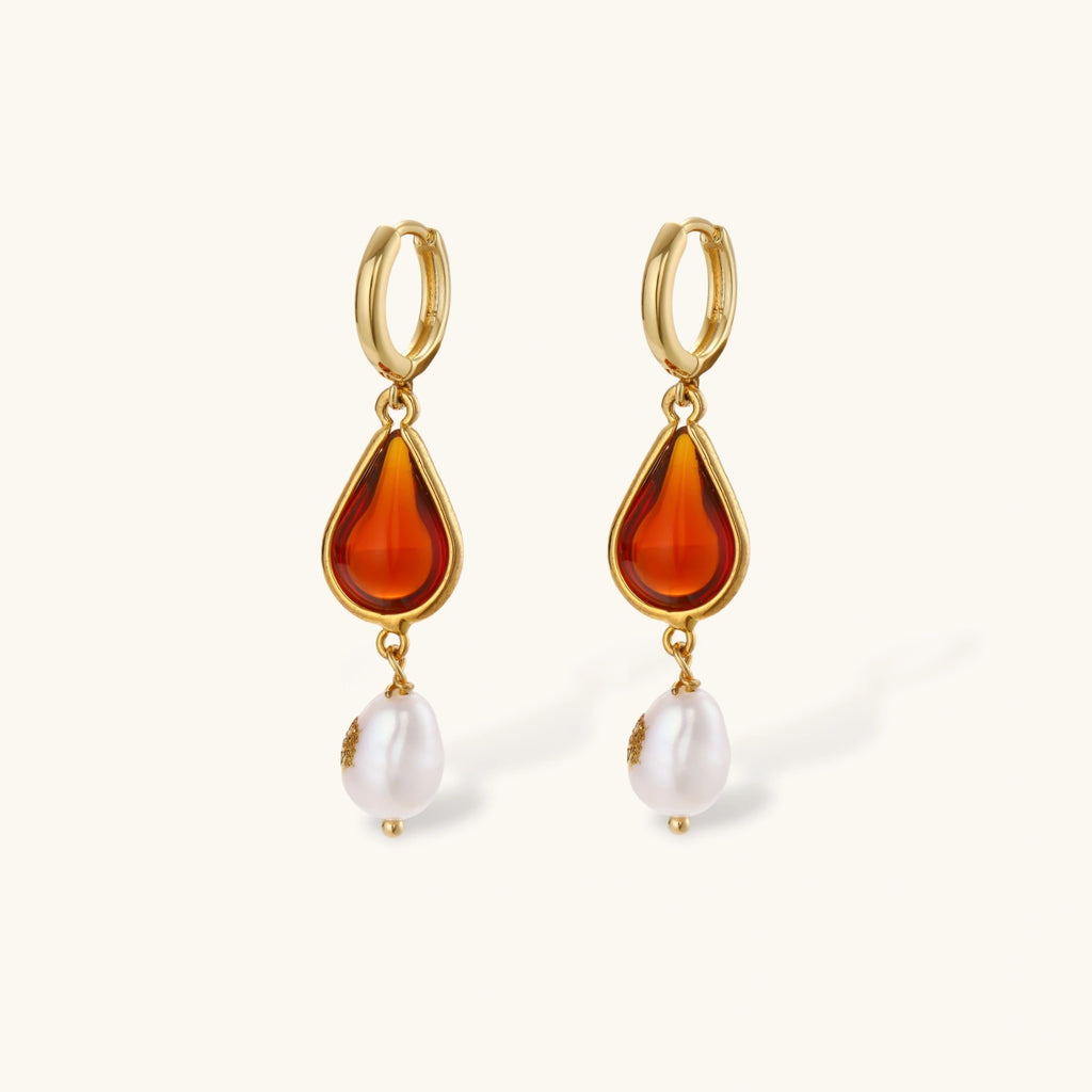 Gold-plated drop earrings featuring amber teardrops and white baroque pearls on light background.