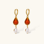 Gold-plated drop earrings featuring amber teardrops and white baroque pearls on light background.