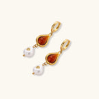 Gold-plated drop earrings featuring amber teardrops and white baroque pearls on light background.