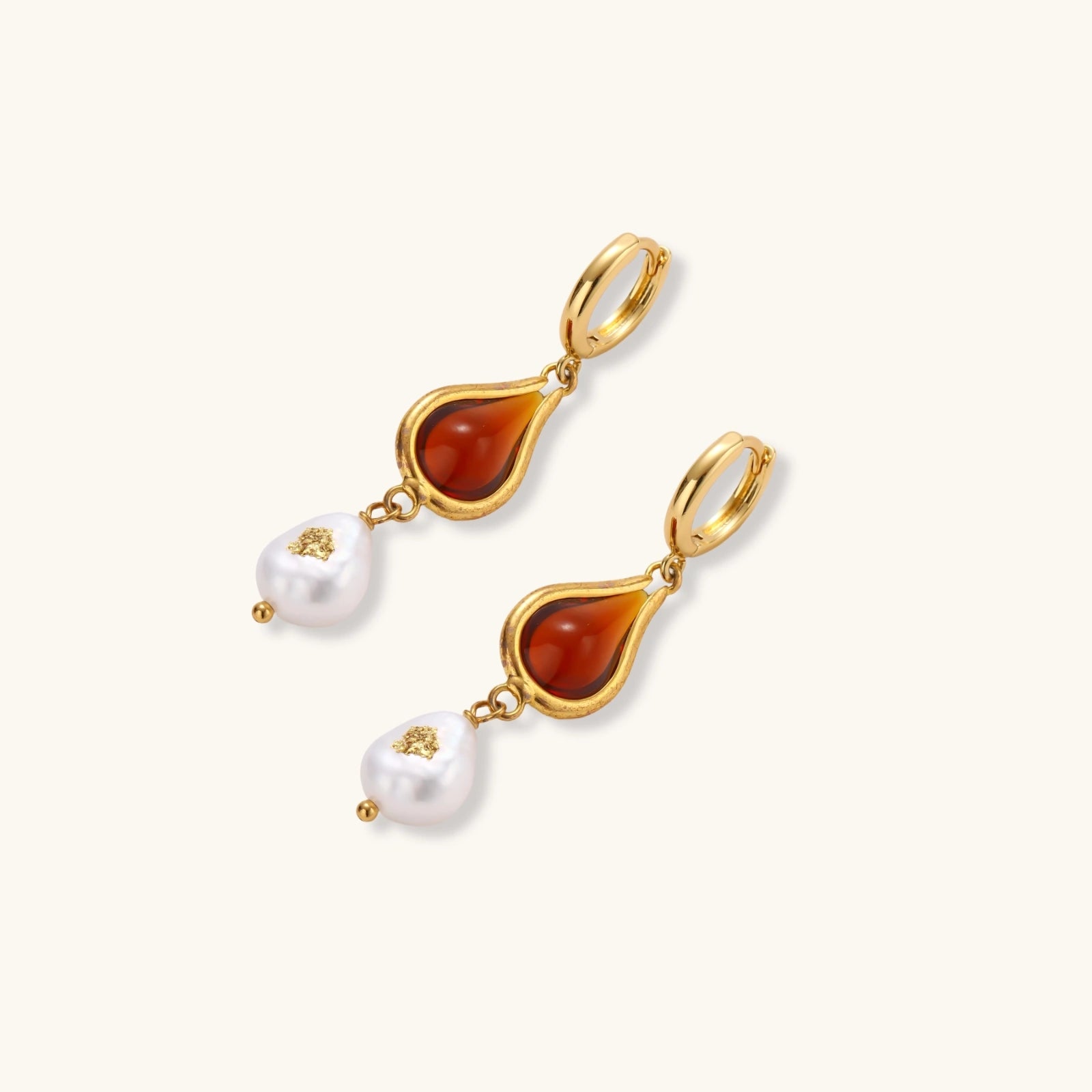 Gold-plated drop earrings featuring amber teardrops and white baroque pearls on light background.