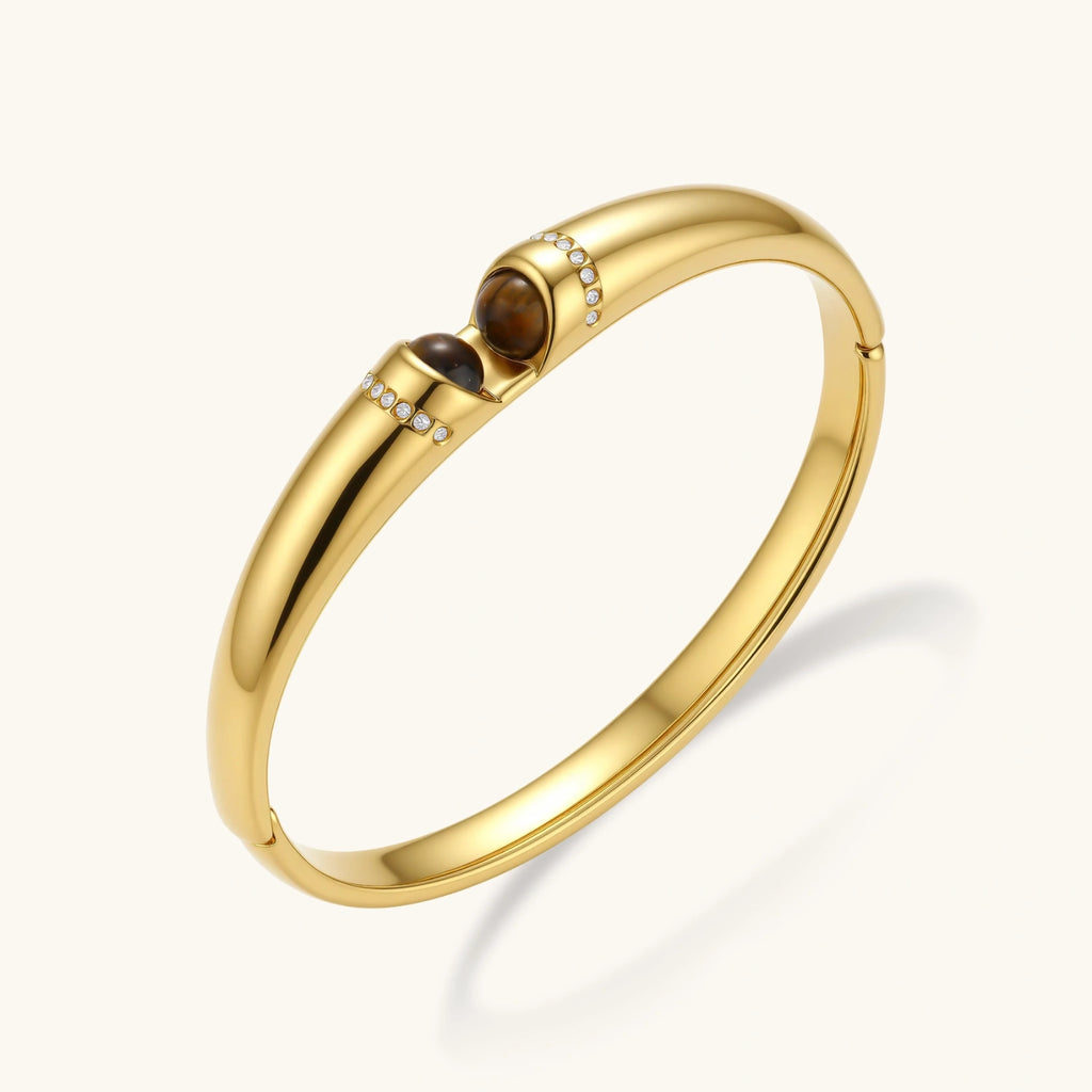 Polished gold bangle with two oval tiger's eye cabochons flanked by pavé diamond accents at center clasp.