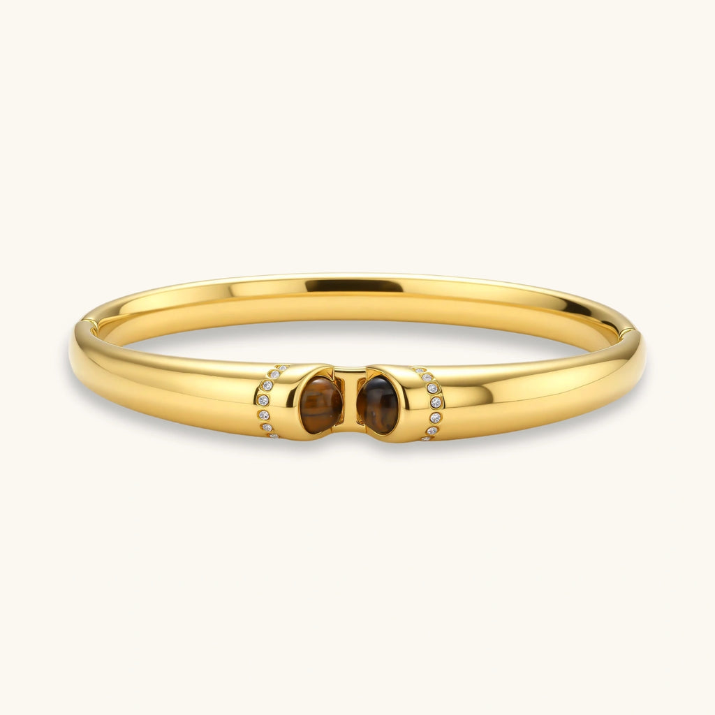 Polished gold bangle with two oval tiger's eye cabochons flanked by pavé diamond accents at center clasp.
