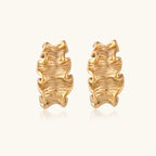 Sculptural gold hoops with textured wave patterns and rippled surface in 14K plating, shown from front and back angles